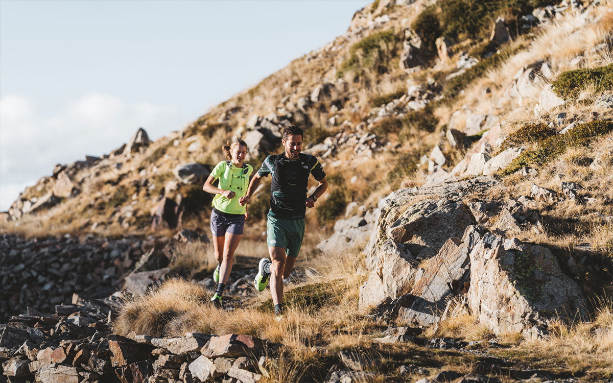 2 ragazzi mentre corrono su un sentiero montano con attrezzatura The North Face da trail running