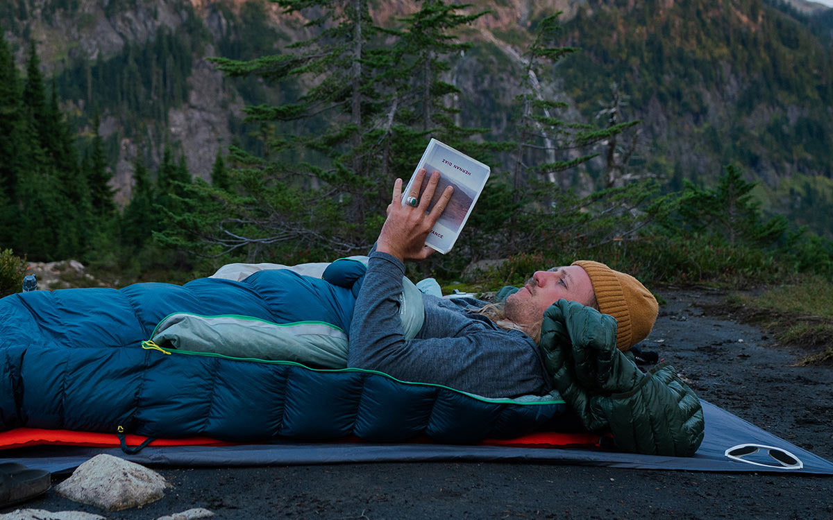 Un ragazzo legge un libro all'aperto nel suo sacco a pelo Therm-a-Rest Questar™