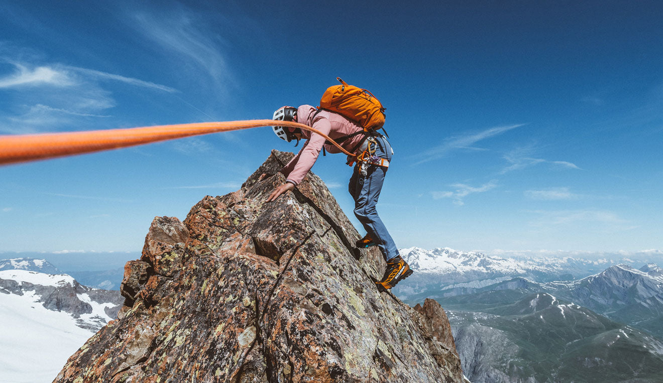 Un alpinista sul picco di una roccia, veste Scarpa