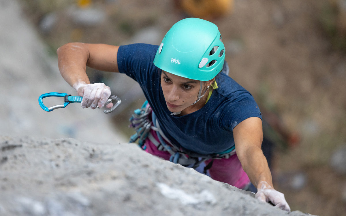 Una ragazza arrampicata su una parete di rocca sta per aggiungere un rinvio Petzl