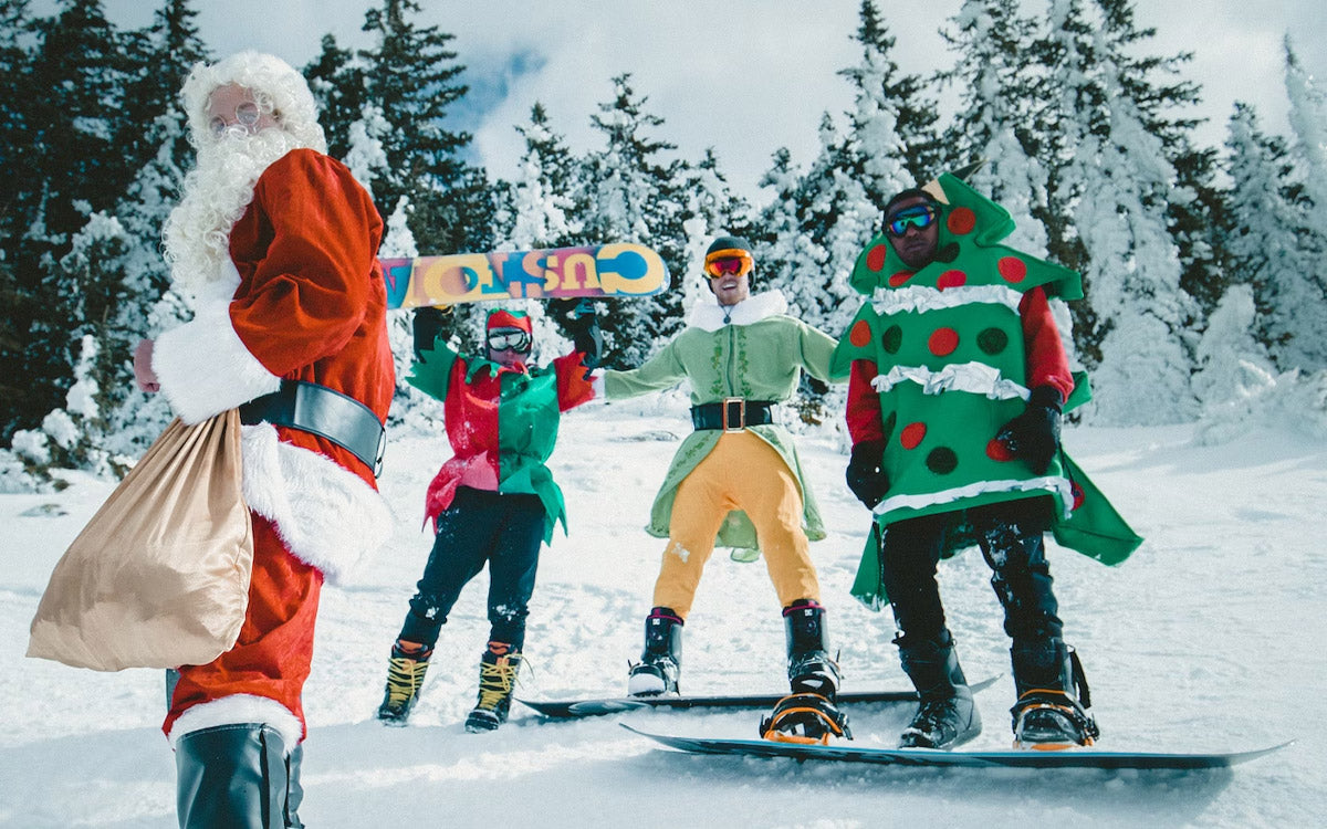 4 ragazzi indossano costumi natalizi sopra l'abbigliamento da snowboard